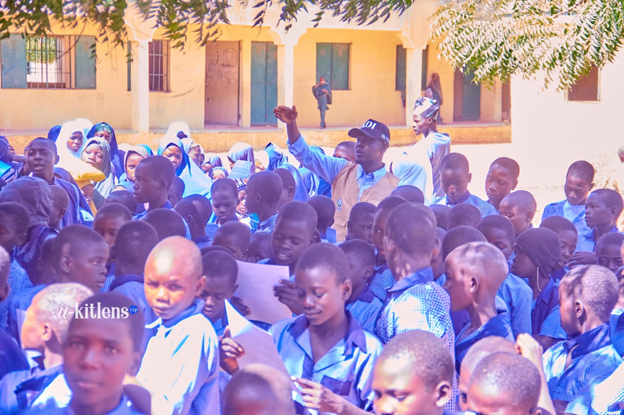 KDI volunteer displaying malaria prevention leaflet in front of student crowd